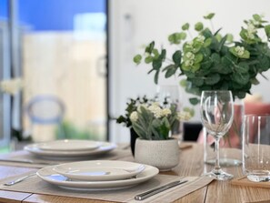 Una mesa de comedor lista con platos, cubiertos y un jarrón con flores.