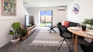 Ein modernes Wohnzimmer mit Fernseher, Sofa, Esstisch und Topfpflanzen.