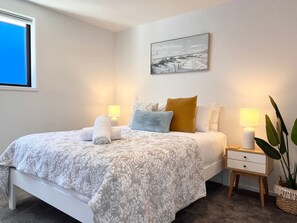 Quarto com cama, luminárias de cabeceira, mesa de apoio, planta em vaso e um quadro na parede.