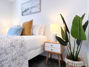 A bedroom with a bed, bedside table, lamp, and a potted plant.