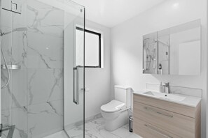 A modern bathroom with a glass shower enclosure, a toilet, and a vanity with a mirror. - Sunny townhouse with parking and EV charging in Christchurch (Christchurch)