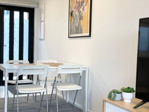 A modern room with a white table and chairs, a framed artwork on the wall, and a small plant on a side table. - Sunny townhouse with parking and EV charging in Christchurch (Christchurch)