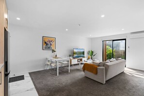 Un salon moderne avec un canapé, une table à manger et des chaises, un téléviseur et un tableau accroché au mur.