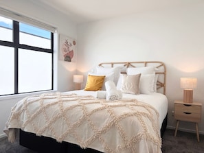 A neatly made bed with a beige and white patterned bedspread, a wooden headboard, and two bedside tables with lamps.