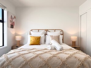 A neatly made bed with a beige and white color scheme, two bedside lamps, and a wall-mounted artwork. - Rattan king-bed retreat with a workspace in Christchurch (Christchurch)