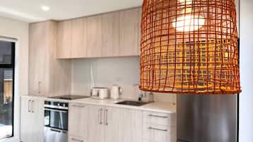 A modern kitchen with light wood cabinets, stainless steel appliances, and a woven orange pendant light.