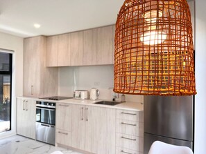 A modern kitchen with light wood cabinets, stainless steel appliances, and a woven orange pendant light. - Rattan king-bed retreat with a workspace in Christchurch (Christchurch)