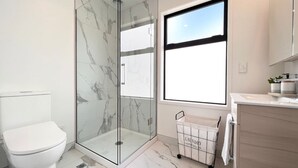 Ein modernes Badezimmer mit einer gläsernen Duschkabine, Toilette und einem Fenster für Tageslicht.