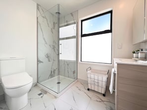 A modern bathroom with a glass-enclosed shower, a toilet, and a window providing natural light.