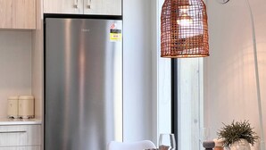 Eine moderne Küche mit einem Edelstahlkühlschrank, einem weißen Esstisch mit Glasplatte und einer hängenden, orangefarbenen Drahtleuchte.