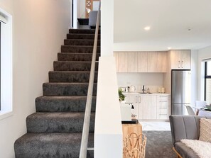 A modern interior with a staircase leading to a kitchen area. - Rattan king-bed retreat with a workspace in Christchurch (Christchurch)