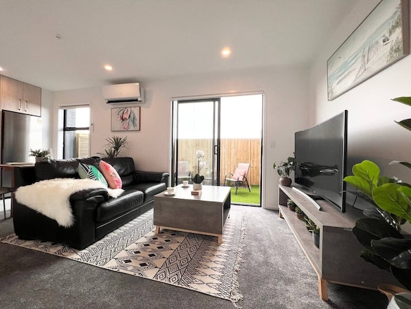 A modern living room with a black leather sofa, a grey coffee table, and a flat-screen TV.