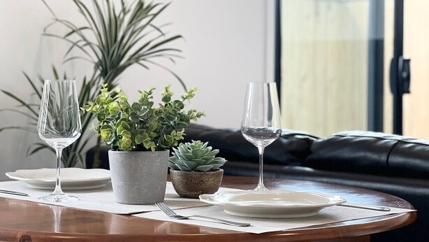 A dining table set with two wine glasses, a plate, and two potted plants.