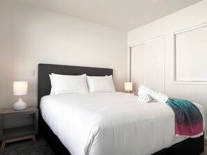 A neatly made bed with white linens, two bedside lamps, and a folded towel on the right side.