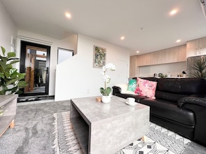 A modern living room with a grey coffee table, a black leather sofa, and a staircase leading to another level.