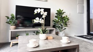 A modern living room with a flat-screen TV, a coffee table with white cups, and potted plants.