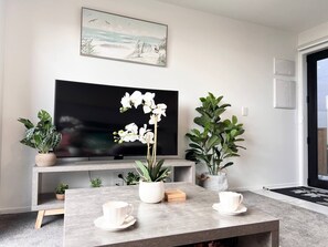 A modern living room with a flat-screen TV, a coffee table with white cups, and potted plants.