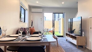 Un salon moderne comprenant un coin repas, un téléviseur et une porte-fenêtre coulissante donnant sur un jardin.