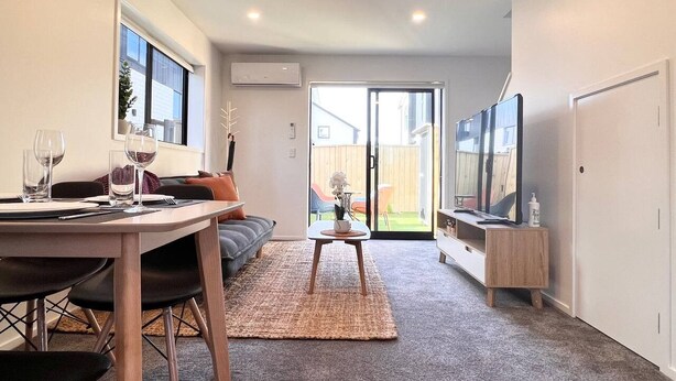 Un salon moderne comprenant un coin repas, un téléviseur et une porte-fenêtre coulissante donnant sur un jardin.