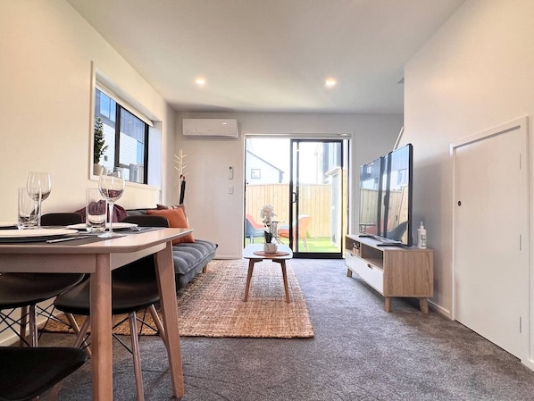 Una sala de estar moderna con comedor, televisor y puerta corrediza de vidrio que da a un patio trasero.