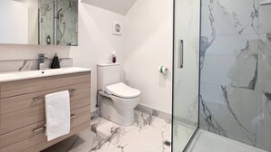 Une salle de bain moderne avec une douche à parois de verre, des toilettes blanches et un meuble-lavabo en bois avec une serviette.