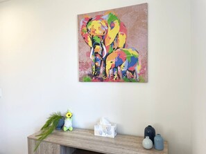 Une pièce comprenant une console en bois, un tableau abstrait aux couleurs vives, une plante en pot et des vases décoratifs.