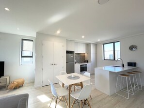 Une cuisine moderne avec des meubles blancs, un coin repas comprenant une table et des chaises blanches, et un petit îlot de cuisine avec des tabourets.