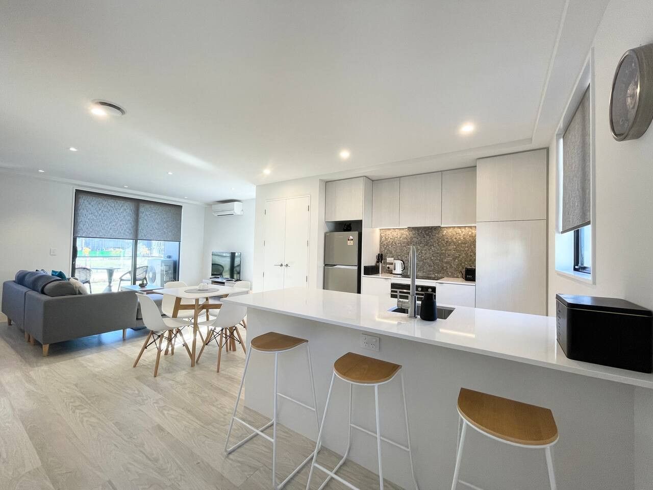 A modern kitchen with a central island, bar stools, and a dining area with a sofa and chairs.