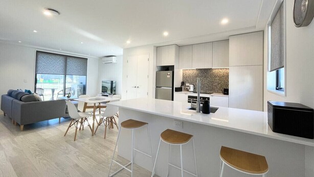 Una cocina moderna con una isla central, taburetes de bar y un comedor con sofá y sillas.