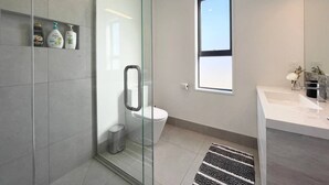 Een moderne badkamer met een douchecabine van glas, een toilet en een wastafel met een marmeren aanrecht.