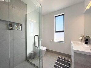 A modern bathroom with a glass shower enclosure, a toilet, and a sink with a marble countertop.
