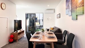 Un salon moderne avec une table à manger pour quatre personnes, un canapé et un téléviseur posé sur un meuble en bois.