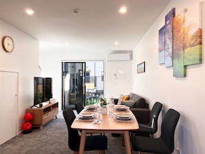 Een moderne woonkamer met een eettafel voor vier personen, een bank en een televisie op een houten kast.