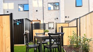 Une terrasse avec une table et des chaises, entourée d’une clôture en bois et d’un petit jardin.