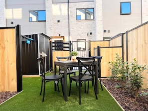 Een terras met een tafel en stoelen, omgeven door een houten omheining en een kleine tuin.