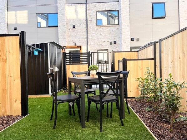 Un patio con una mesa y sillas, rodeado por una valla de madera y un pequeño jardín.