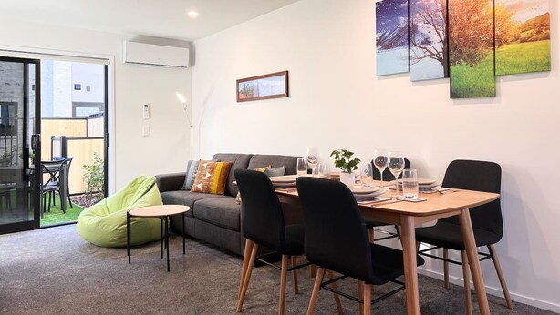 Un salon moderne avec un canapé, une table à manger et des chaises, ainsi qu’un fauteuil en forme de haricot vert. Trois tableaux ornent le mur et une fenêtre offre une vue sur l’extérieur.