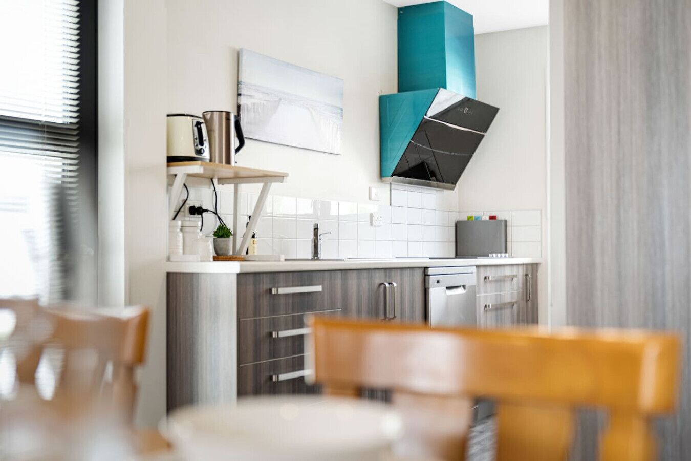 Una cocina moderna con azulejos blancos, electrodomésticos de acero inoxidable y una pared de acento color aguamarina.