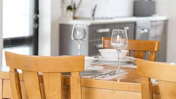 Una mesa de comedor de madera con dos copas de vino y un bol, ubicada en una cocina moderna con armarios blancos y una ventana.
