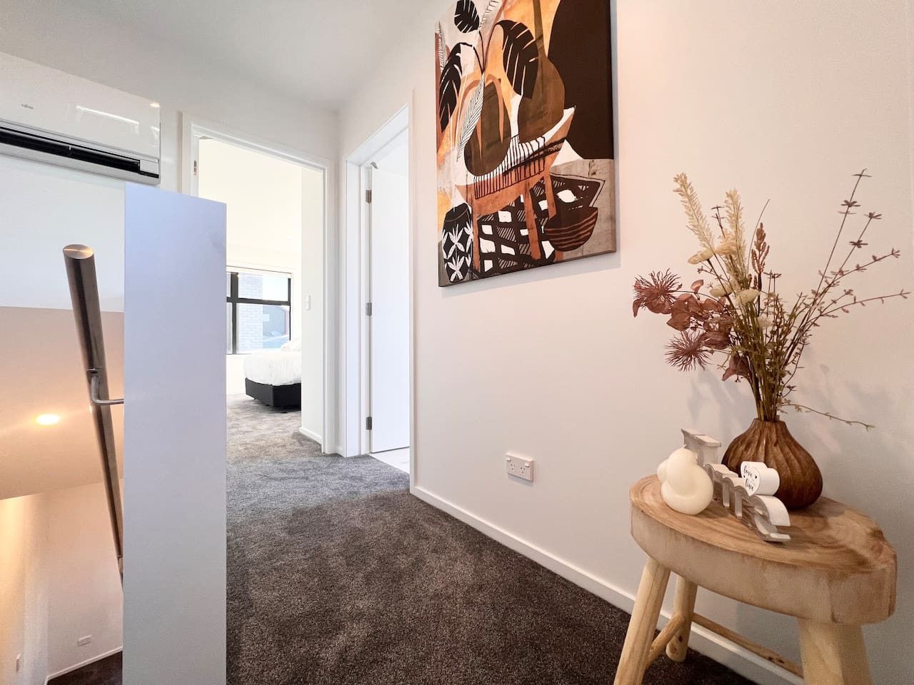 A hallway with a modern kitchen area, a dining table, and a decorative wall piece.