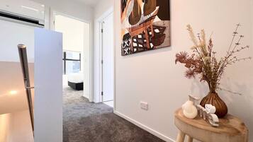 A hallway with a modern kitchen area, a dining table, and a decorative wall piece.