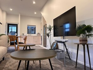 Una sala moderna con un televisor de pantalla plana, una mesa de centro redonda, un sofá y un comedor con sillas.