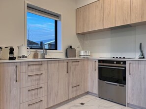 A modern kitchen with light wood cabinetry, a built-in oven, and a window overlooking a snowy landscape.