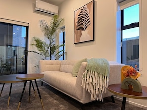 A living room with a sofa, a round coffee table, a potted plant, and a framed artwork on the wall.