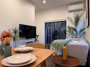 A modern living room with a flat-screen TV, a dining table set with plates and cutlery, a sofa, and a large window. - Lichfield city stay with a super king suite in Christchurch (Christchurch)
