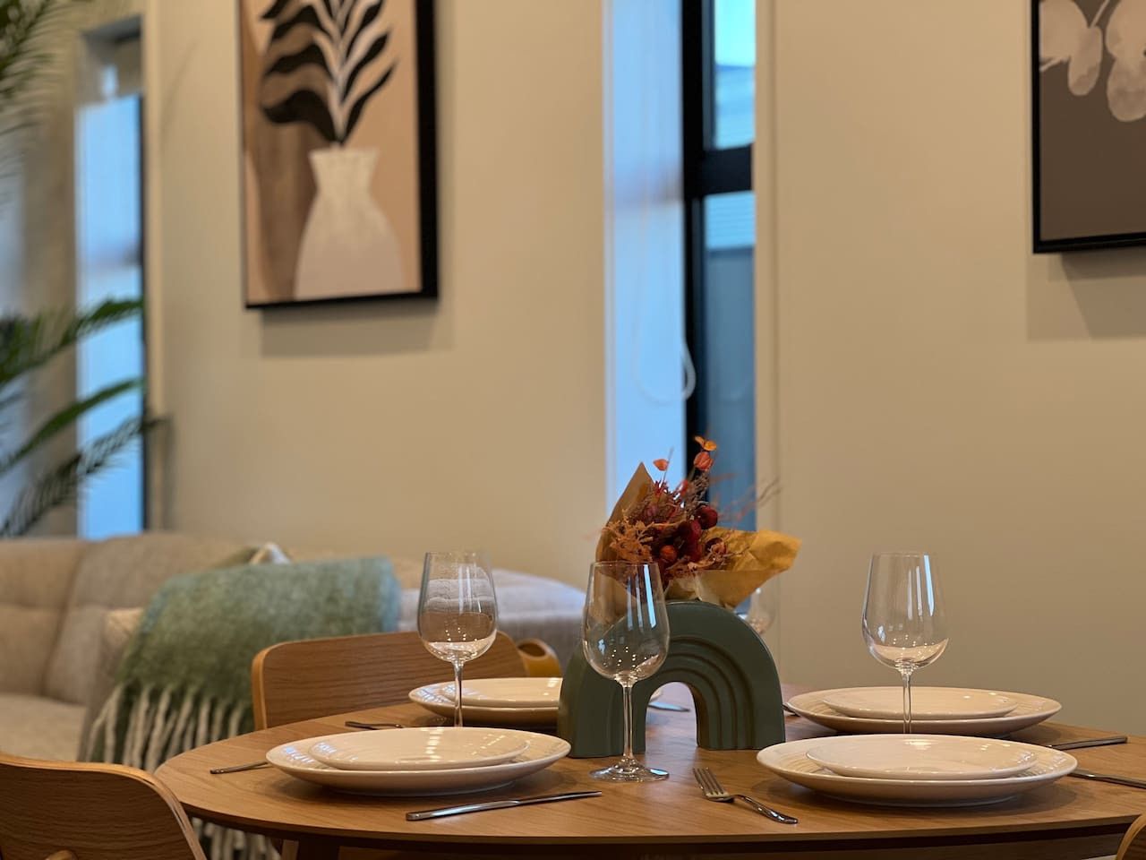 A dining table set with plates, wine glasses, and cutlery, with a vase of flowers and a decorative bowl in the center.