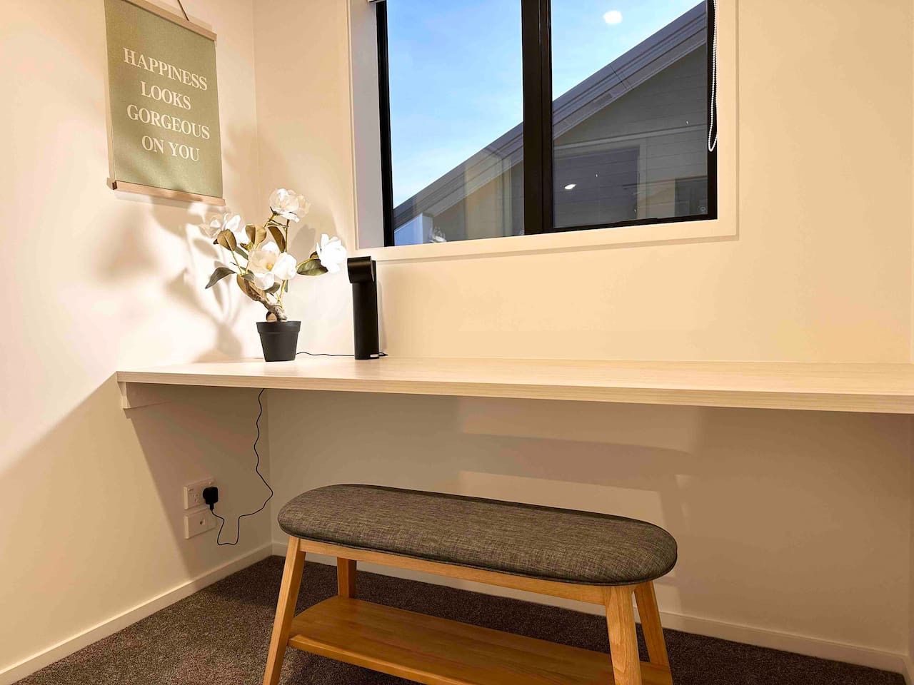 A room with a desk, a bench, a potted plant, and a motivational quote on the wall.