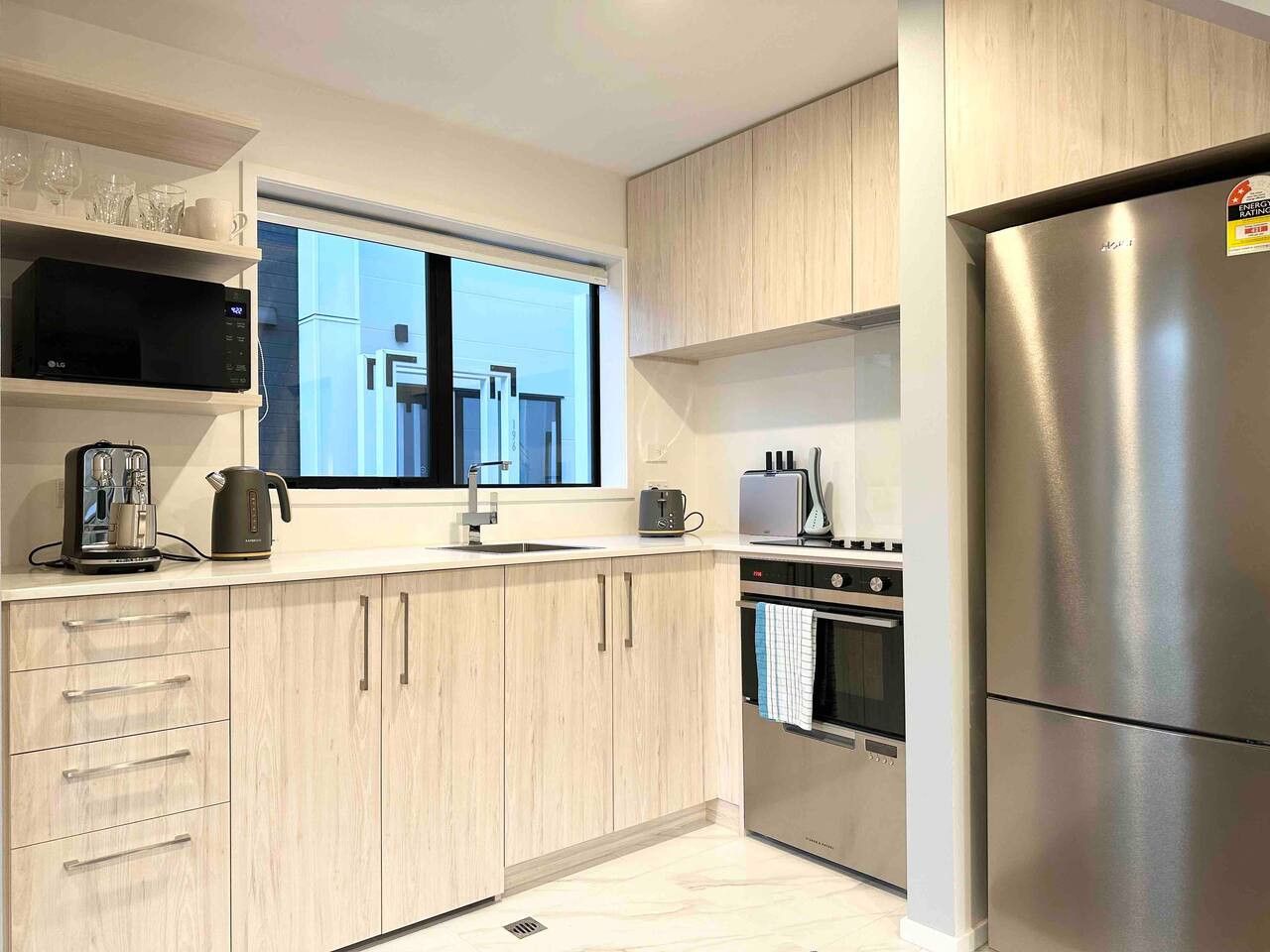 A modern kitchen with light wood cabinets, stainless steel appliances, and a window providing natural light.