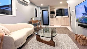 Sala de estar moderna com sofá, mesa de centro de vidro e cozinha ao fundo.