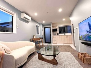 Una sala moderna con un sofá, una mesa de centro de vidrio y una cocina al fondo.